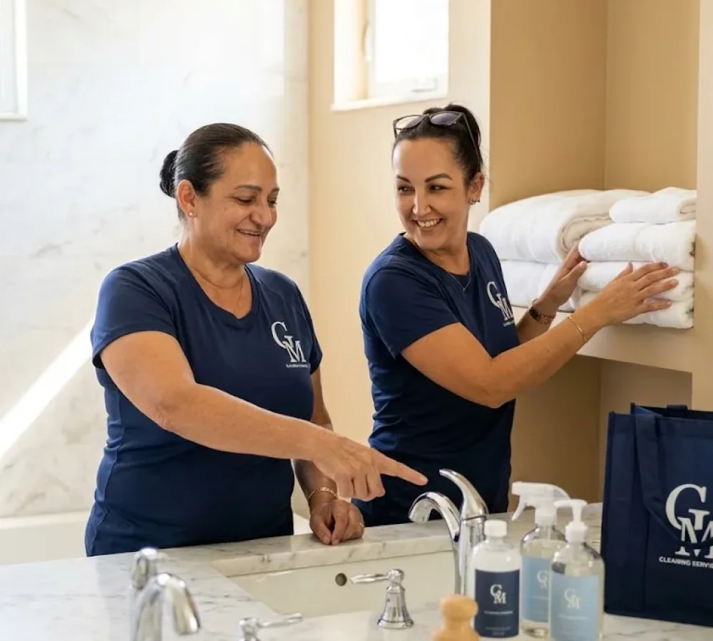 Two Cleaning Services GM team members restocking fresh towels and cleaning supplies in a Florida Keys vacation rental bathroom during a turnover clean